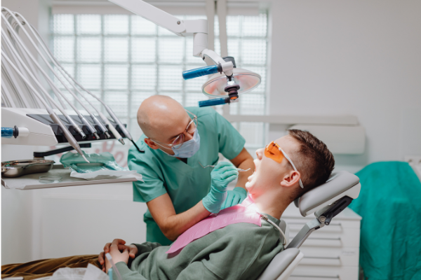 A smiling male patient in a dental chair during a comprehensive oral exam with a dentist using a dental mirror and explorer.
