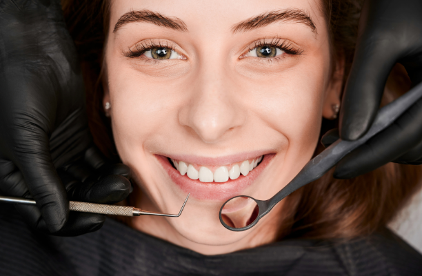 A smiling female patient in a dental chair looking at the camera while a dentist prepares to perform a targeted checkup.