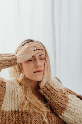 A woman holding her forehead and jaw, expressing discomfort from a tension headache often associated with TMD.