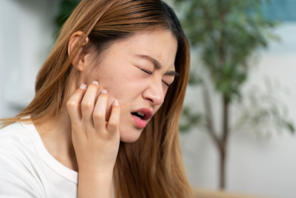 A woman squinting in discomfort while touching the side of her face to indicate sharp jaw pain.