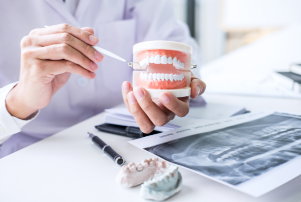 A dentist's hands holding a dental model while reviewing an X-ray and dental casts on a desk.
